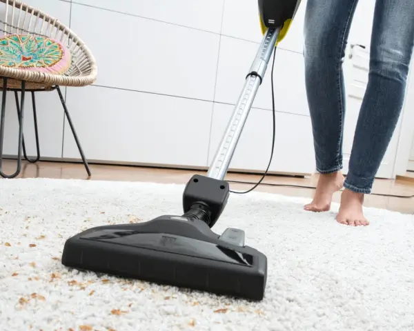 Eine Person saugt mit einem Sapur Teppichreiniger einen weißen Teppich ab. Die Anleitung ist hier nicht sichtbar, aber das Ergebnis wird sauber sein.
