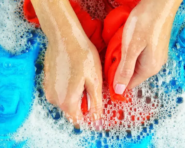 Hände waschen rote und blaue Sportsachen in schaumigem Wasser.