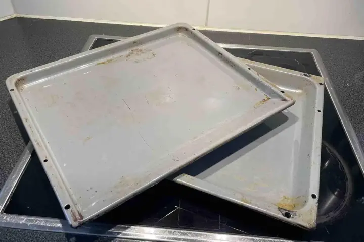 Zwei alte, graue Backbleche mit Gebrauchsspuren und Verfärbungen liegen übereinander auf einem Cerankochfeld. Zeit, das Backblech reinigen!