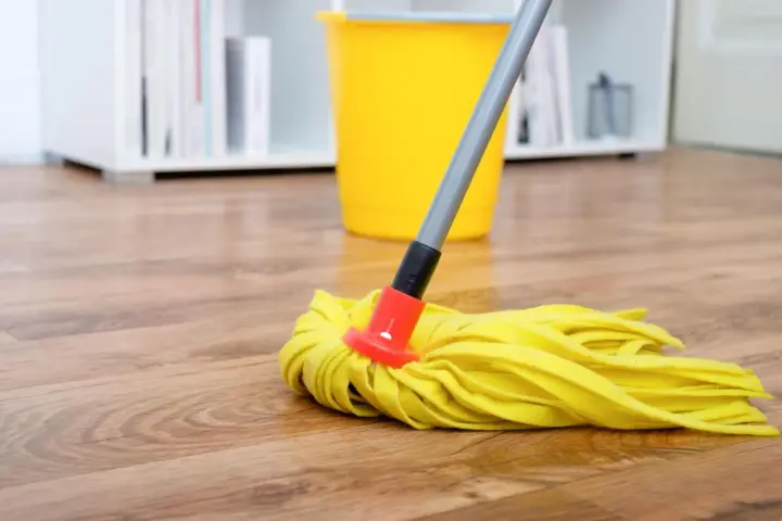 Gelber Wischmopp auf Laminatboden, bereit für die Reinigung mit Hausmitteln. Ein gelber Eimer steht im Hintergrund.