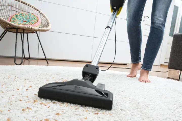 Eine Person saugt mit einem Sapur Teppichreiniger einen weißen Teppich ab. Die Anleitung ist hier nicht sichtbar, aber das Ergebnis wird sauber sein.