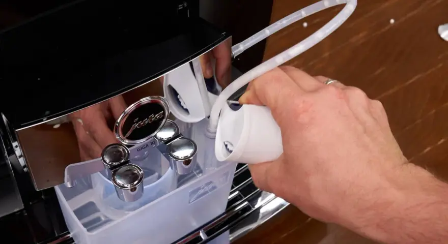 Hand gießt Flüssigkeit in einen Schlauch, um die Kaffeemaschine zu entkalken.