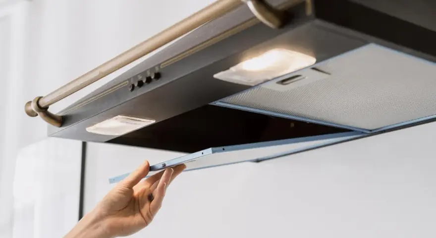 Hand entfernt Fettfilter einer Dunstabzugshaube, um die klebrige Dunstabzugshaube reinigen zu können.