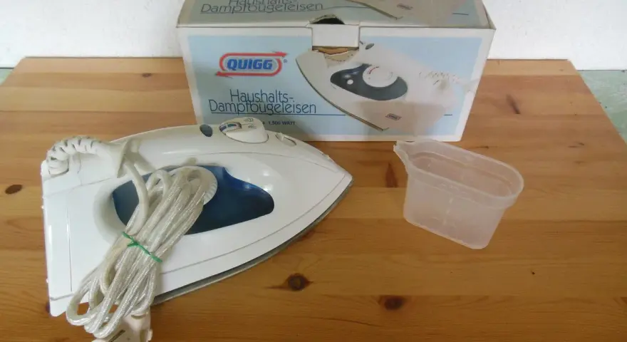 Ein Quigg Dampfbügeleisen mit Zubehör und Verpackung auf einem Holztisch.