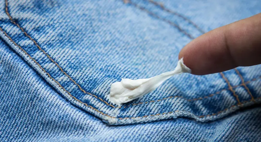 Finger versucht, Kaugummi aus Jeans zu entfernen. Der klebrige weiße Klumpen haftet an der blauen Denim-Oberfläche.