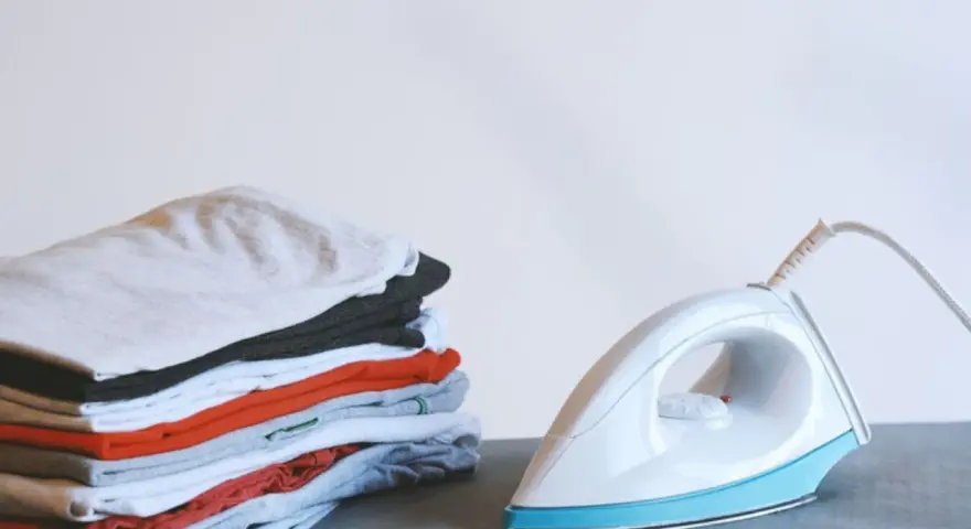 Ein Stapel bunter Kleidung neben einem weißen, easy home bügeleisen.