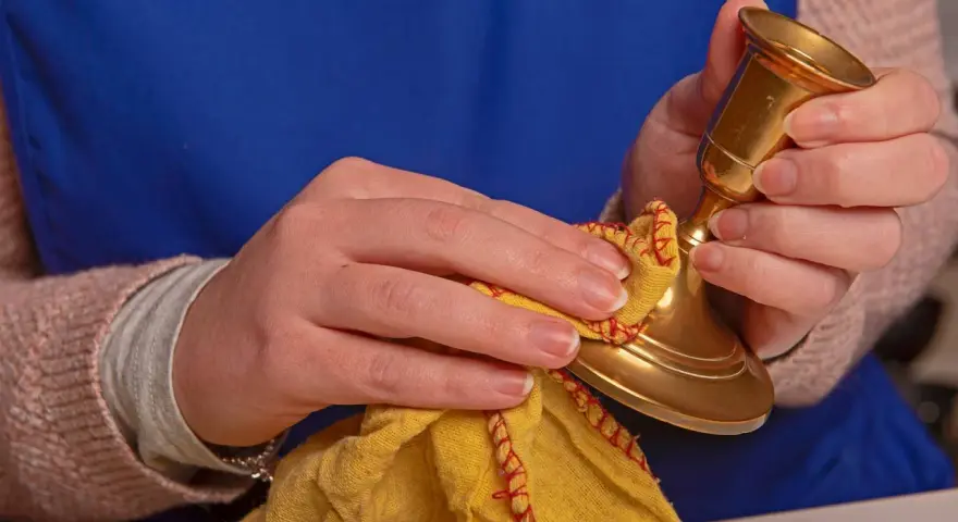 Hände polieren einen goldenen Kerzenständer mit einem gelben Tuch. Messing reinigen für neuen Glanz.
