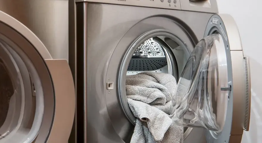 Waschmaschine mit offener Tür und grauen Handtüchern. Perfekt, um hartnäckige colaflecken entfernen zu lassen.