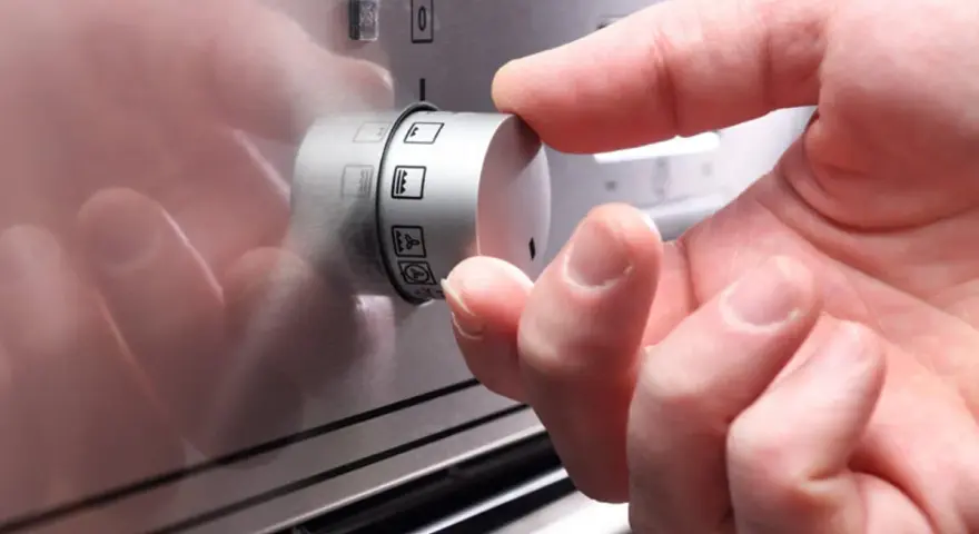 Hand dreht Regler mit Backofen Symbolen.