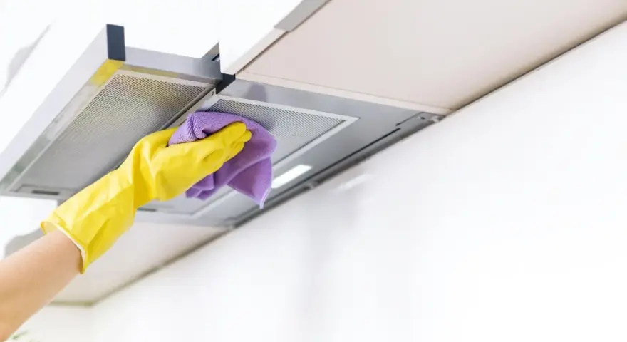 Gelbe Handschuhe wischen mit einem lila Tuch über die Dunstabzugshaube. Alu reinigen für strahlenden Glanz in der Küche.