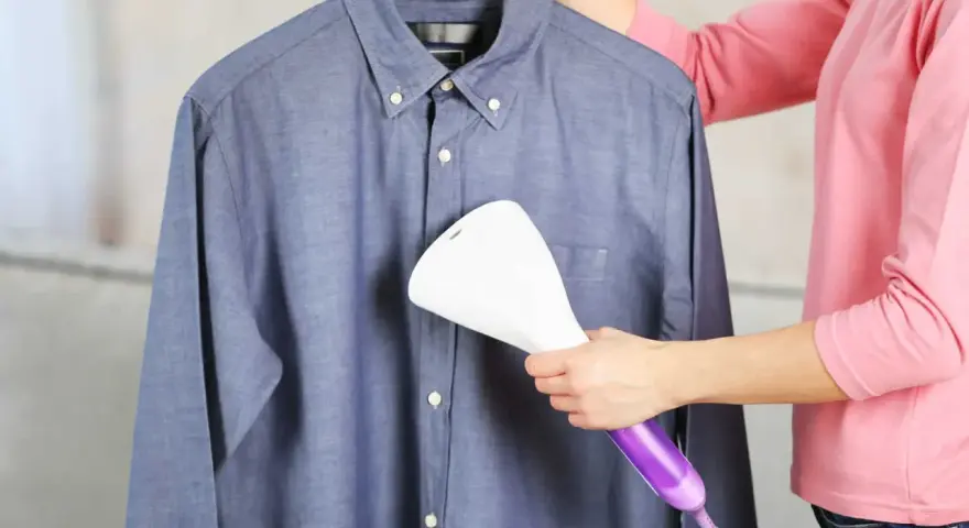 Dampfsteamer test: Eine Person glättet ein blaues Hemd mit einem Handdampfglätter.