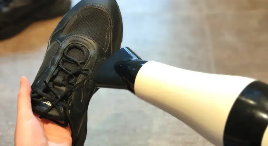 Schwarze Turnschuhe trocknen mit einem Föhn. Ein Paar nasse Schuhe wird mit einem Föhn getrocknet, um sie schnell wieder einsatzbereit zu machen.