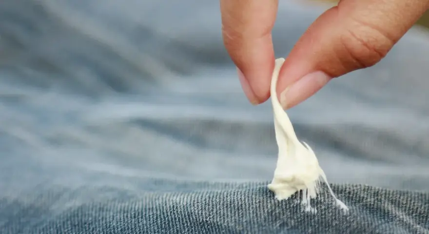 Finger zieht zähen Kaugummi aus Jeansstoff. Ein ärgerliches Malheur, das jeder kennt: Kaugummi aus Kleidung entfernen.