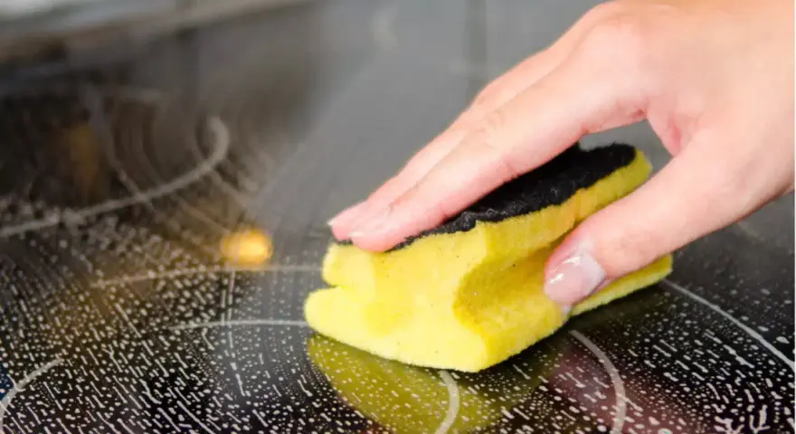 Hand reinigt mit Schwamm und Schaum das Ceranfeld.