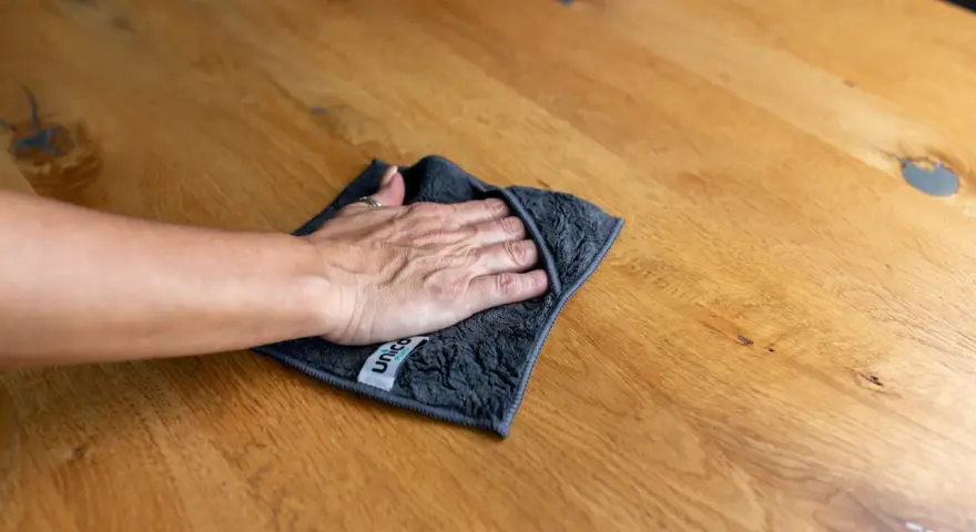 Hand wischt mit Tuch über Holzoberfläche, um Wasserflecken zu entfernen.