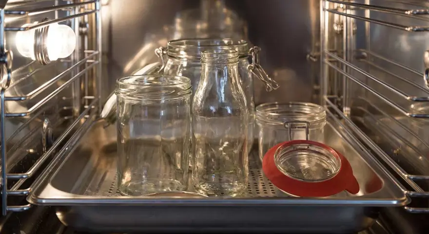 Mehrere leere Gläser und Flaschen stehen auf einem Blech im Backofen, bereit zum Sterilisieren.