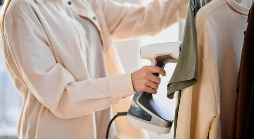 Frau testet Dampfbügler an Kleidung. Schnell und einfach Falten entfernen.