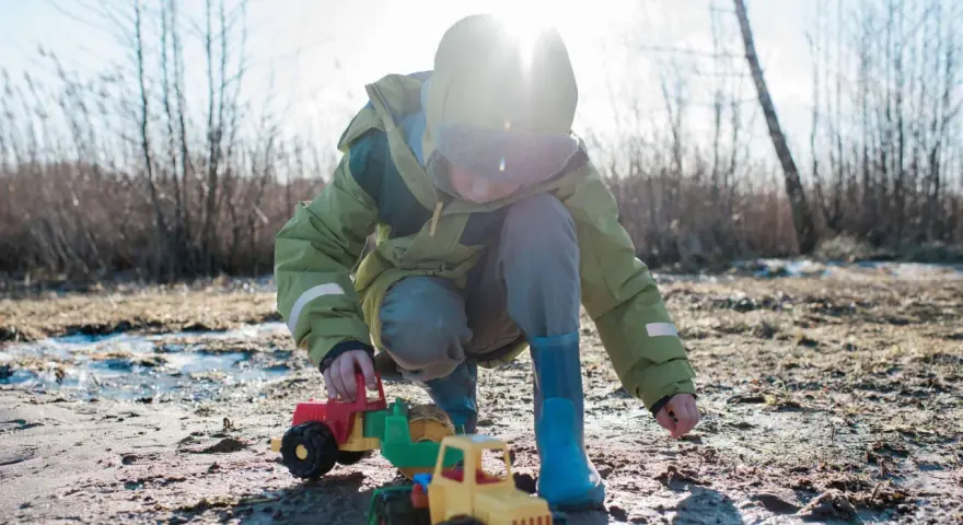 Kind spielt mit Spielzeugtraktoren im Matsch. Die Kleidung wird wohl bald eine Wäsche brauchen, um die matschflecken entfernen zu können.