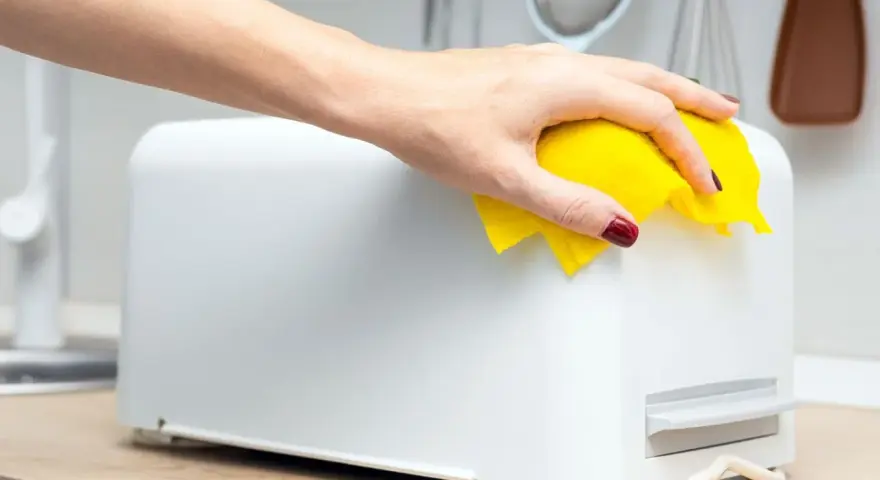 Eine Hand mit gelbem Tuch wischt über einen weißen Toaster. So einfach kann toaster reinigen sein.