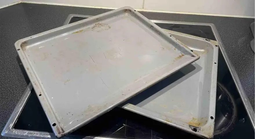 Zwei alte, graue Backbleche mit Gebrauchsspuren und Verfärbungen liegen übereinander auf einem Cerankochfeld. Zeit, das Backblech reinigen!