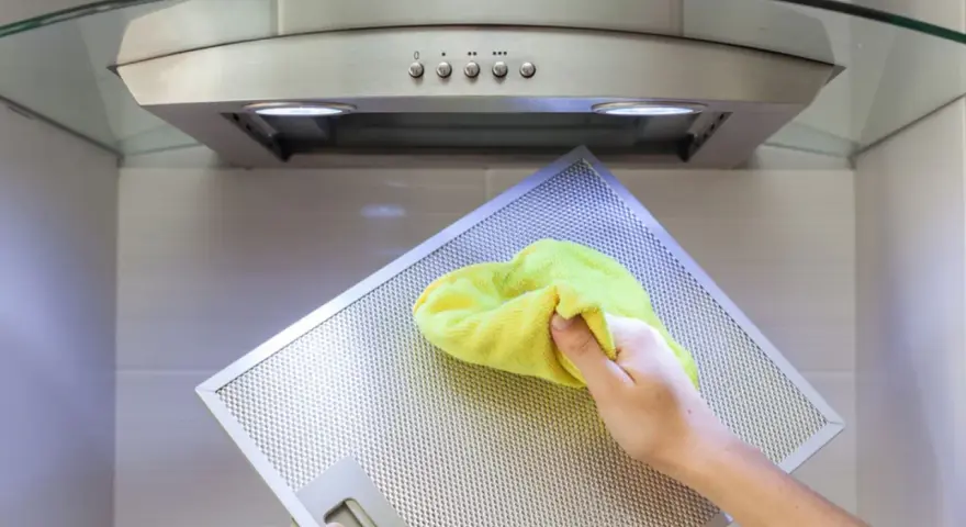Hand reinigt Dunstabzugshaube mit gelbem Tuch.