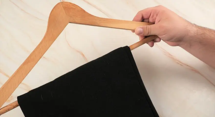 Hand hält einen Holz-Kleiderbügel mit einer schwarzen Anzughose. Zeit, die Anzughose zu waschen.