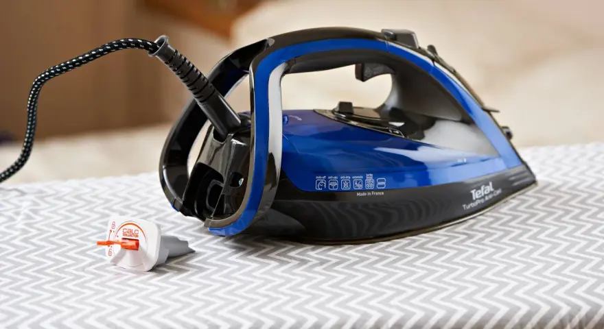 Ein Tefal Bügeleisen mit blauem Wassertank steht auf einem Bügelbrett. Der Stecker ist eingesteckt, aber das Bügeleisen scheint Wasser zu verlieren.