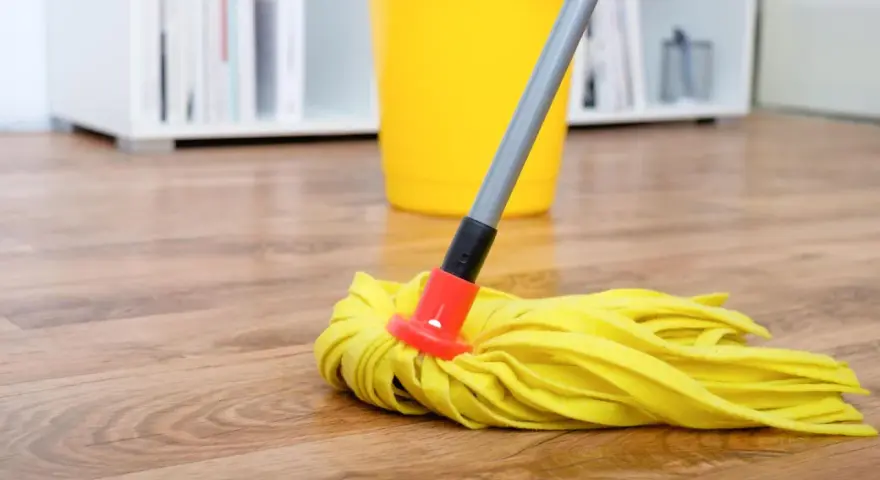 Gelber Wischmopp auf Laminatboden, bereit für die Reinigung mit Hausmitteln. Ein gelber Eimer steht im Hintergrund.