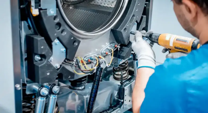 Techniker repariert die Schleudermechanik einer Waschmaschine mit einem Schrauber.