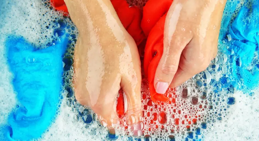 Hände waschen rote und blaue Sportsachen in schaumigem Wasser.
