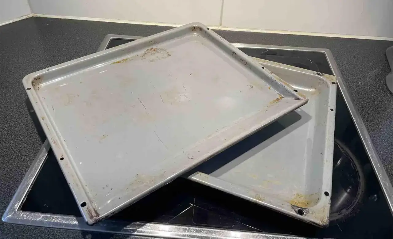 Zwei schmutzige Backbleche liegen auf einem Cerankochfeld. Zeit, das Backblech reinigen!