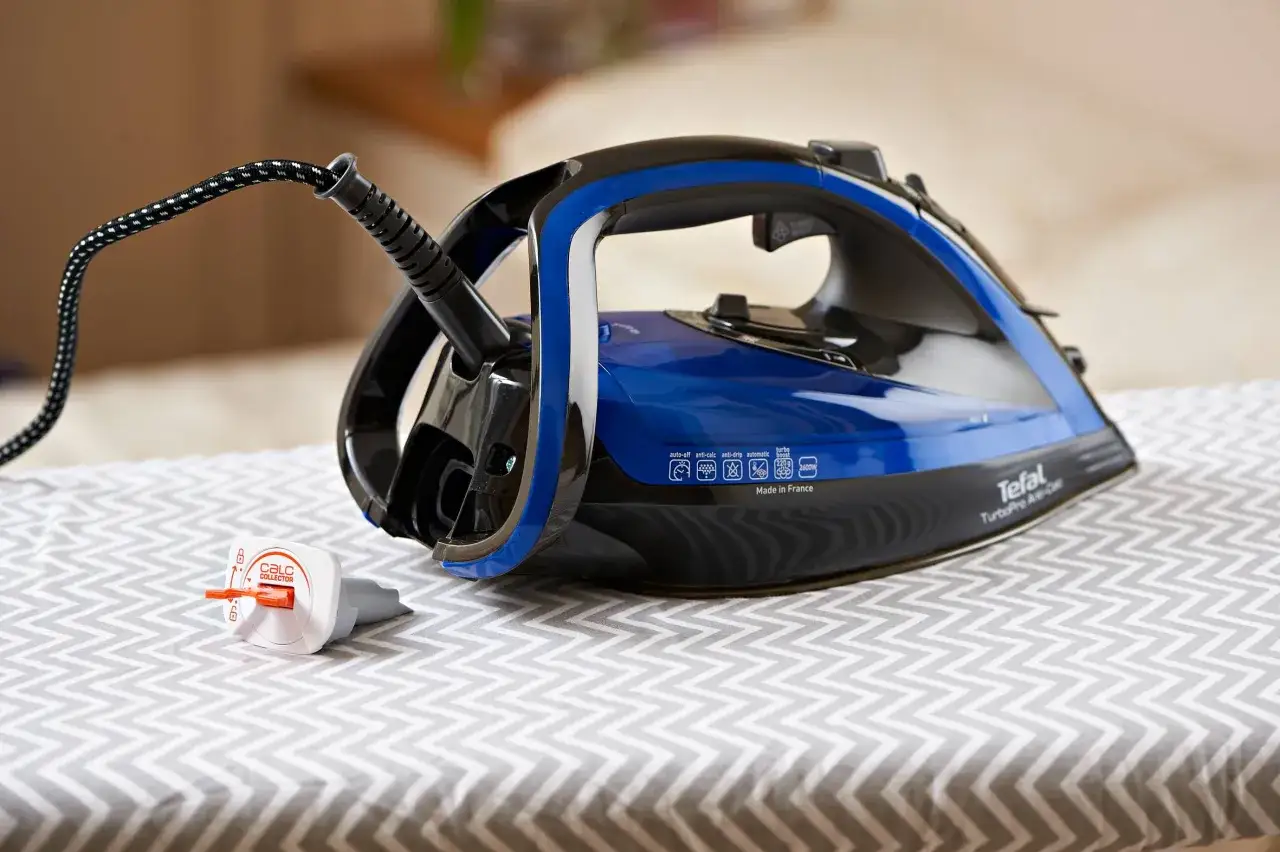 Ein Tefal B&uuml;geleisen mit blauem Wassertank steht auf einem B&uuml;gelbrett. Der Stecker ist eingesteckt, aber das B&uuml;geleisen scheint Wasser zu verlieren.