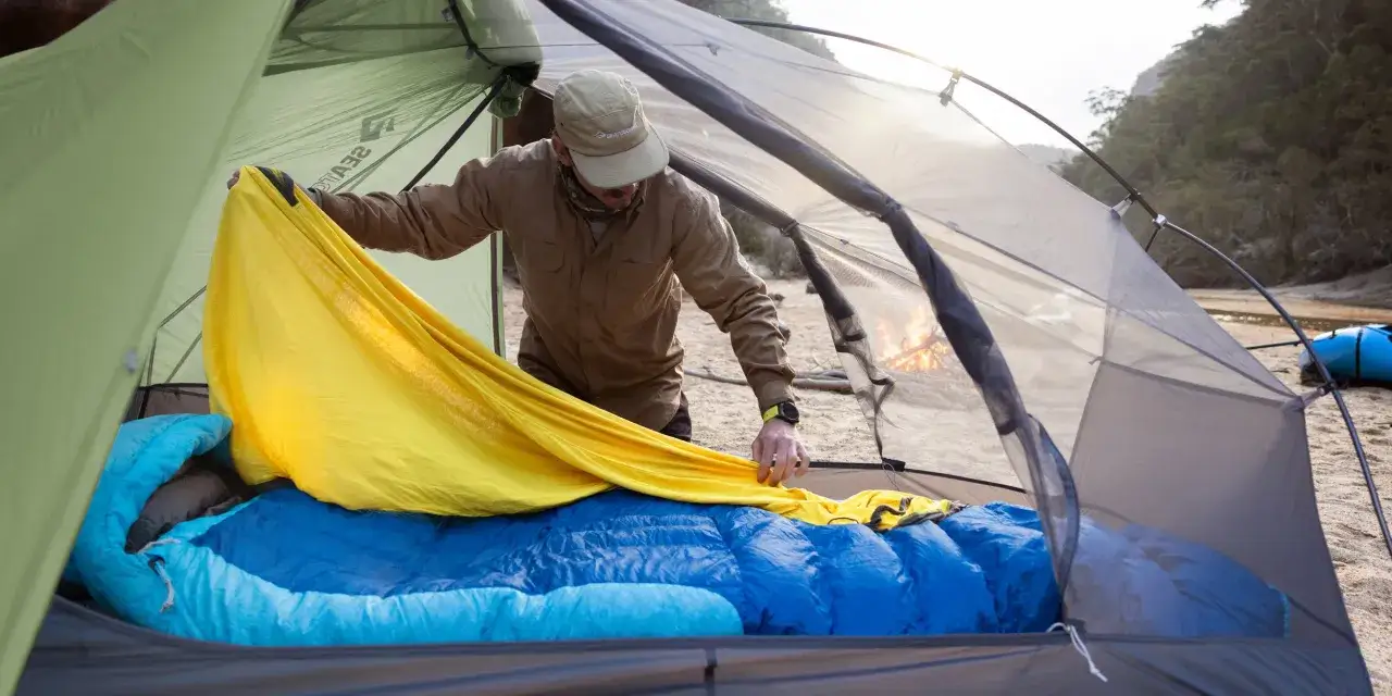 Mann richtet gelbes Tuch im Zelt, um es zu reinigen. Blaue Schlafs&auml;cke liegen bereit.