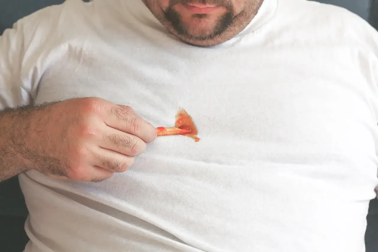 Mann mit Pommes und Ketchup auf wei&szlig;em T-Shirt. Ein Kampf gegen hartn&auml;ckige teeflecken entfernen beginnt.