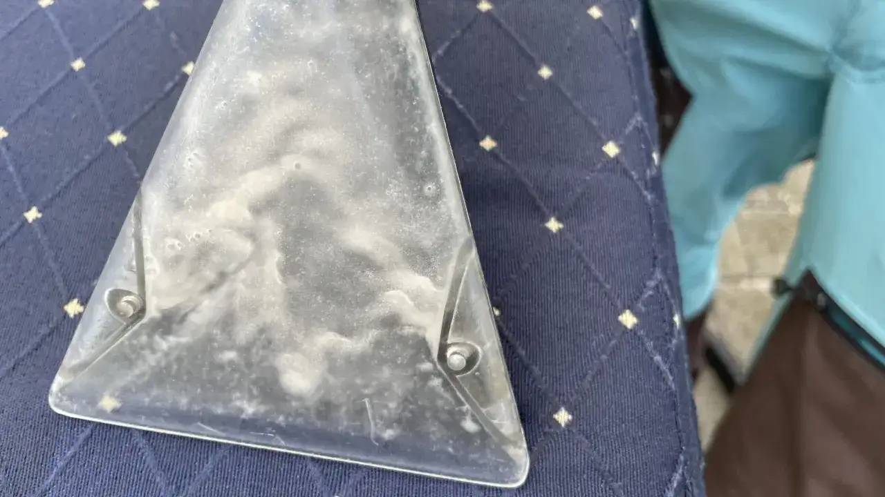 Der transparente Aufsatz eines Sapur Teppichreinigers mit Schaumresten liegt auf einem dunkelblauen Teppich.