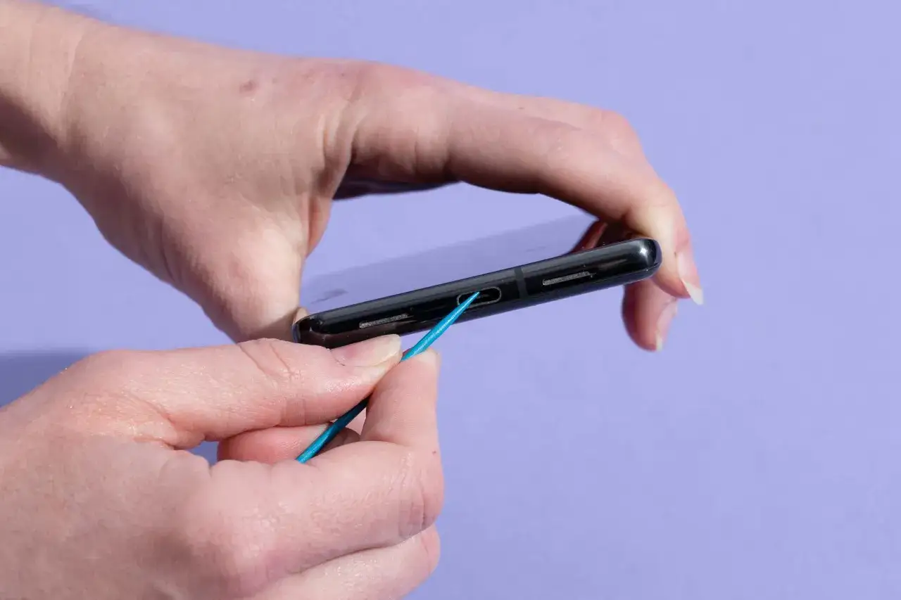 H&auml;nde reinigen das Handy mit einem blauen Werkzeug.