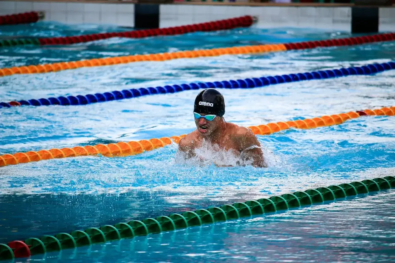 Schwimmer mit Arena-Kappe und Schwimmbrille, der im Wettkampf schwimmt. Die Schwimmbrille reinigen ist wichtig f&uuml;r klare Sicht.