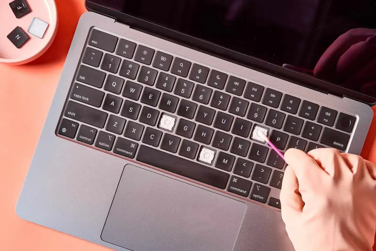 Eine Hand reinigt mit einem Wattest&auml;bchen die Tasten eines Laptops. Die Tastenkappen von 