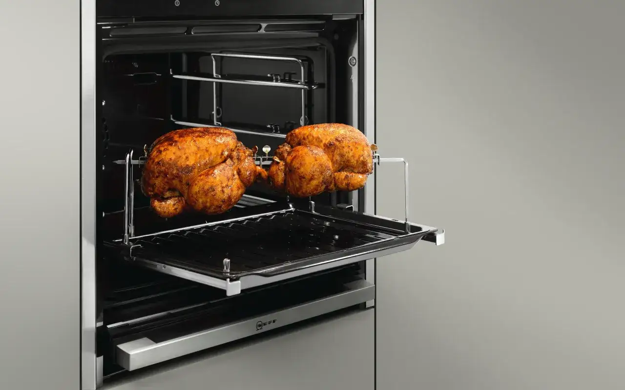 Zwei goldbraune H&auml;hnchen drehen sich auf einem Drehspie&szlig; im Backofen. Die Grillfunktion sorgt f&uuml;r perfekte Br&auml;une.