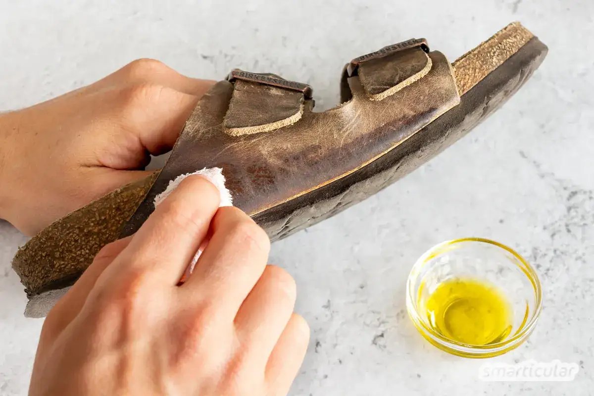 H&auml;nde reinigen eine braune Birkenstock-Sandale mit einem Tuch. Ein kleines Sch&auml;lchen mit &Ouml;l steht daneben. So gelingt das Birkenstock reinigen.