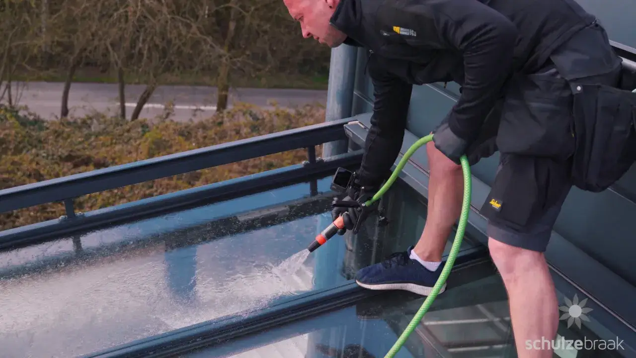 Mann reinigt mit Gartenschlauch von unten das Glasdach.