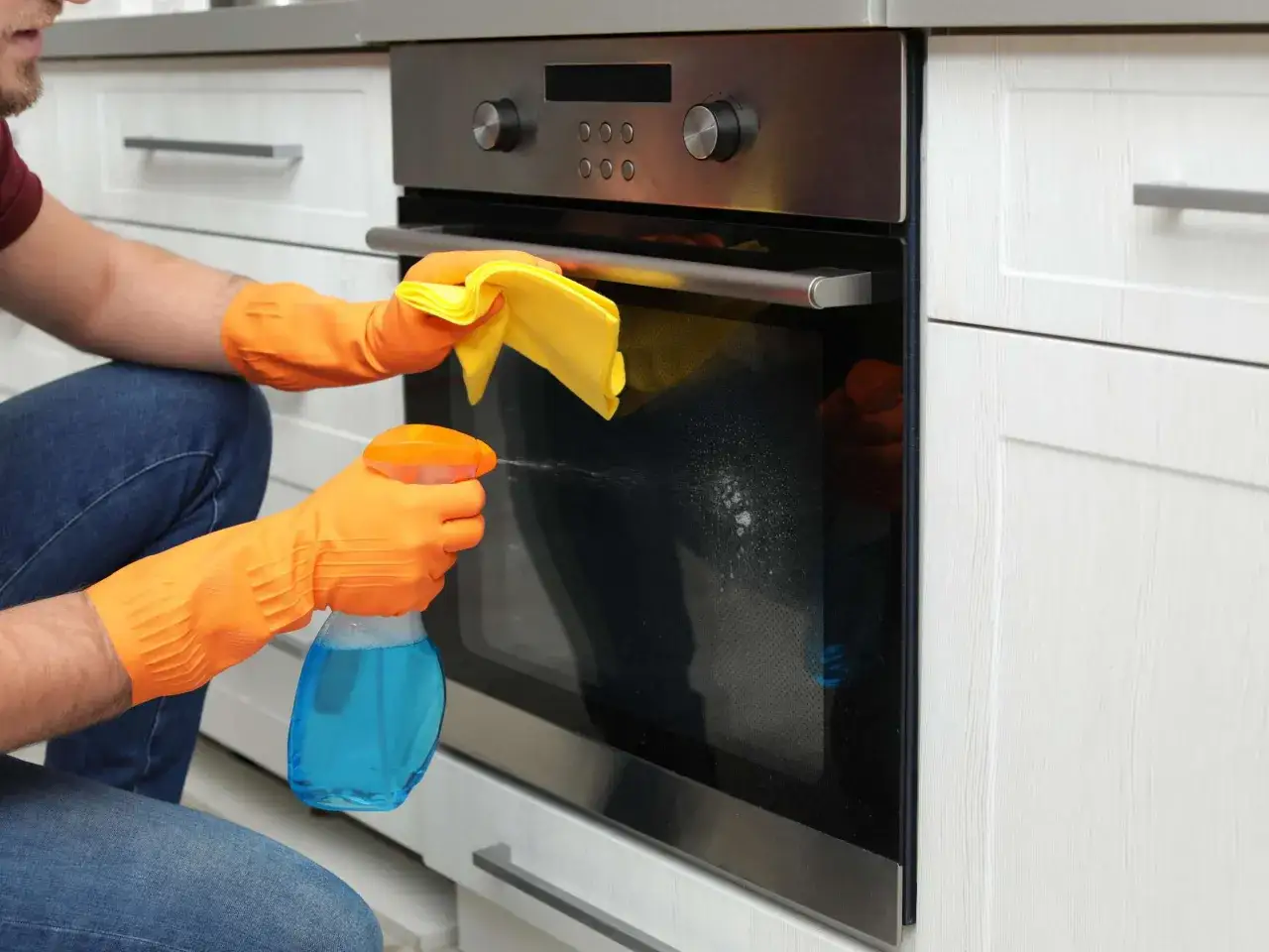 Mann reinigt die Backofen-Zwischenscheibe ohne Ausbau mit Spr&uuml;hreiniger und gelbem Tuch.