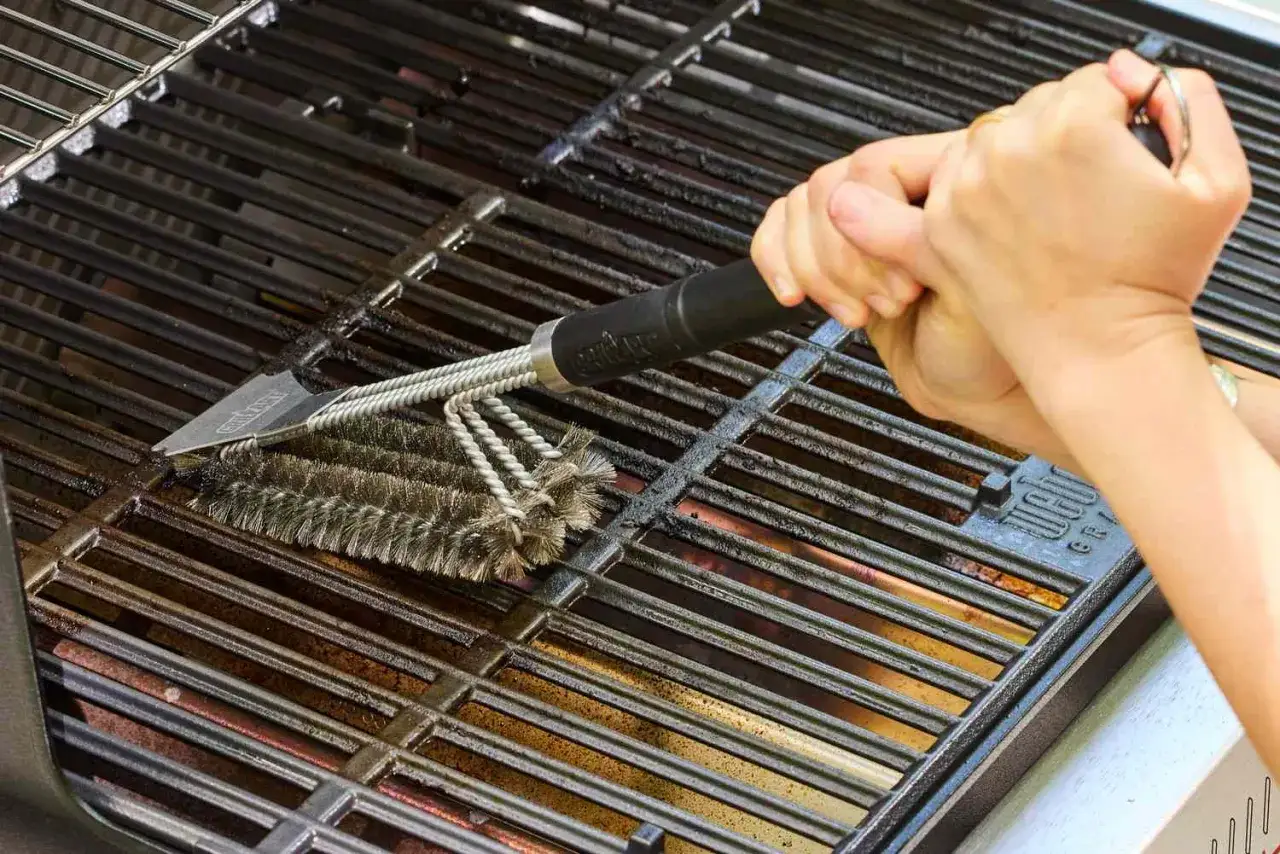 Hände reinigen mit einer Grillbürste den schmutzigen Grillrost.