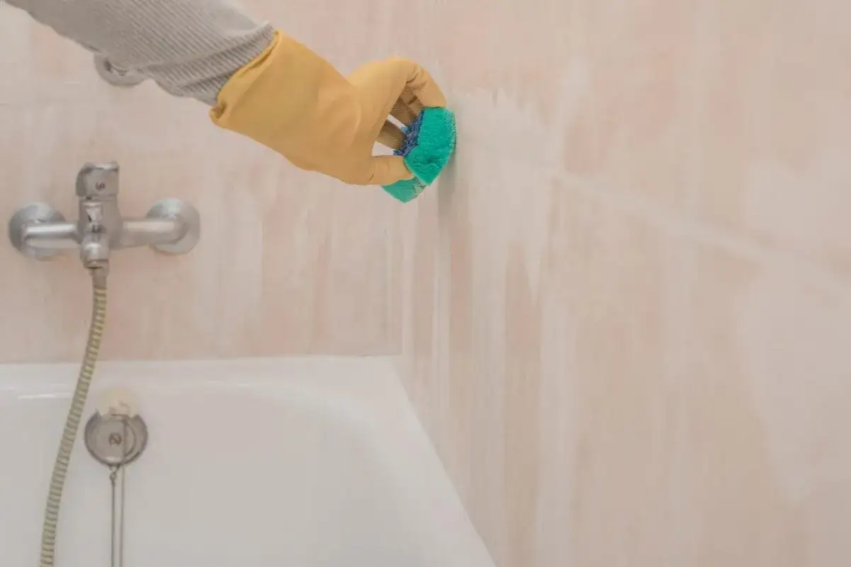 Mit gelben Handschuhen werden die hellrosa Badfliesen gereinigt. Ein gr&uuml;ner Schwamm schrubbt hartn&auml;ckigen Schmutz weg.
