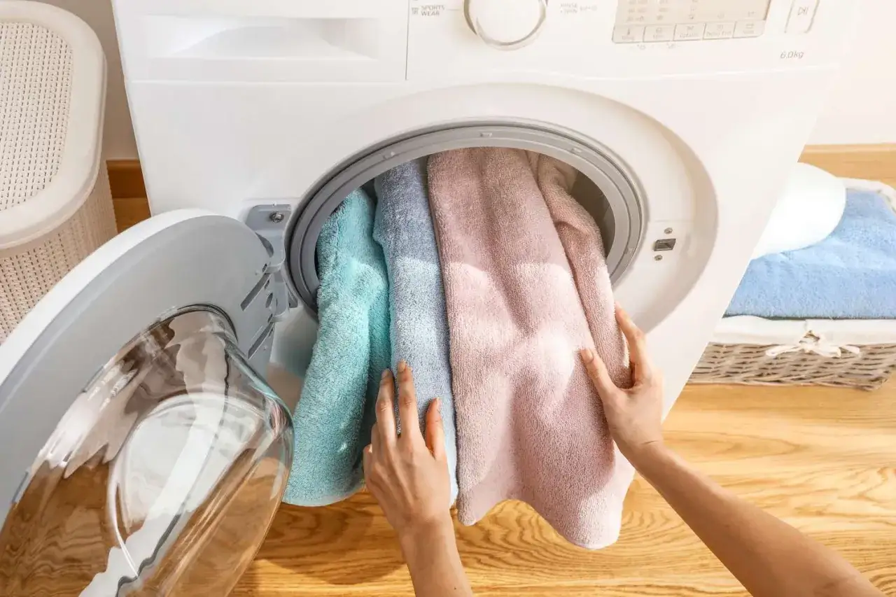 Hände legen bunte Handtücher zum Handtuch waschen in die Waschmaschine.