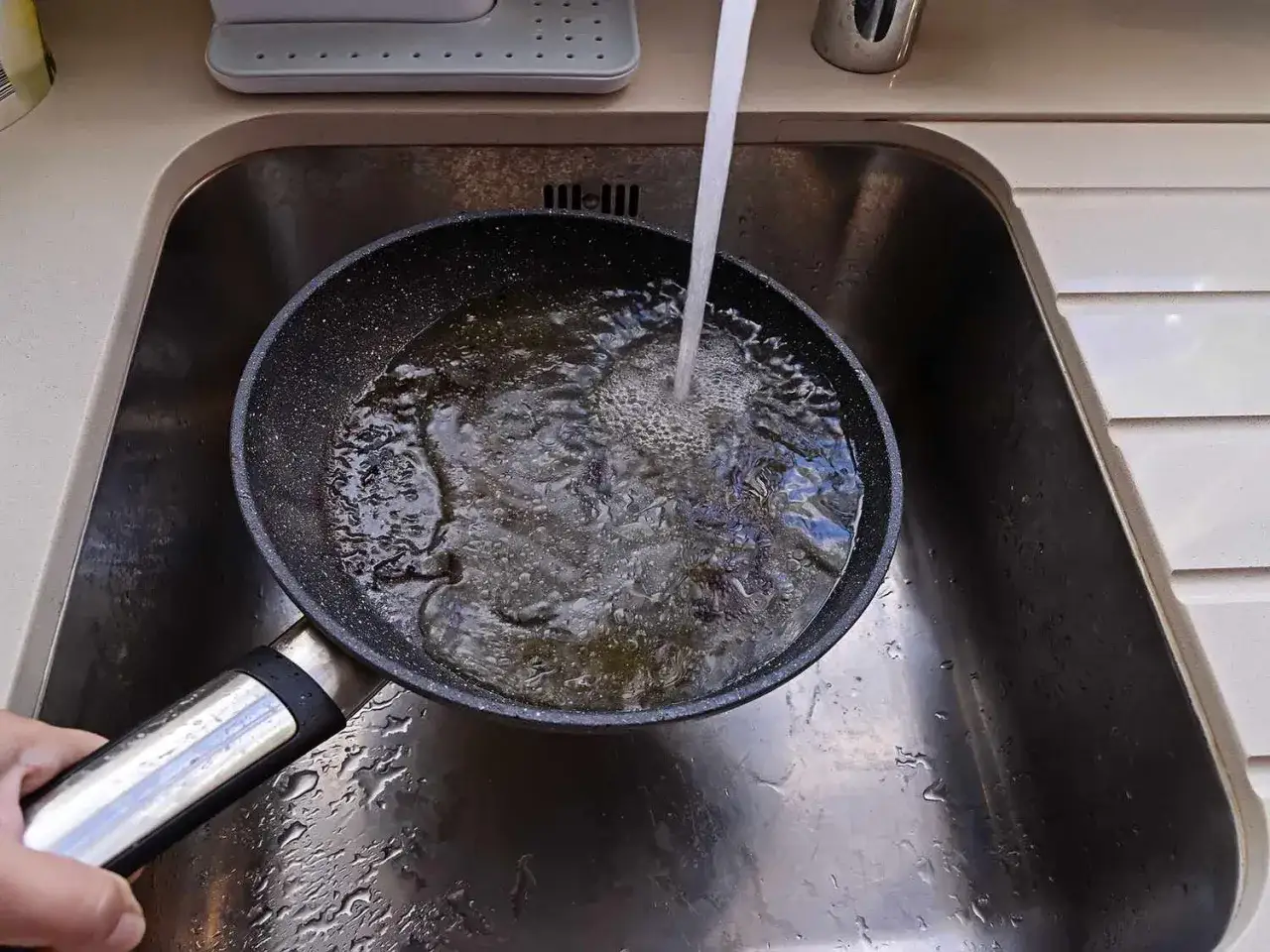 Eine beschichtete Pfanne reinigen: Wasser l&auml;uft in die Pfanne in der Sp&uuml;le, um Fett zu l&ouml;sen.