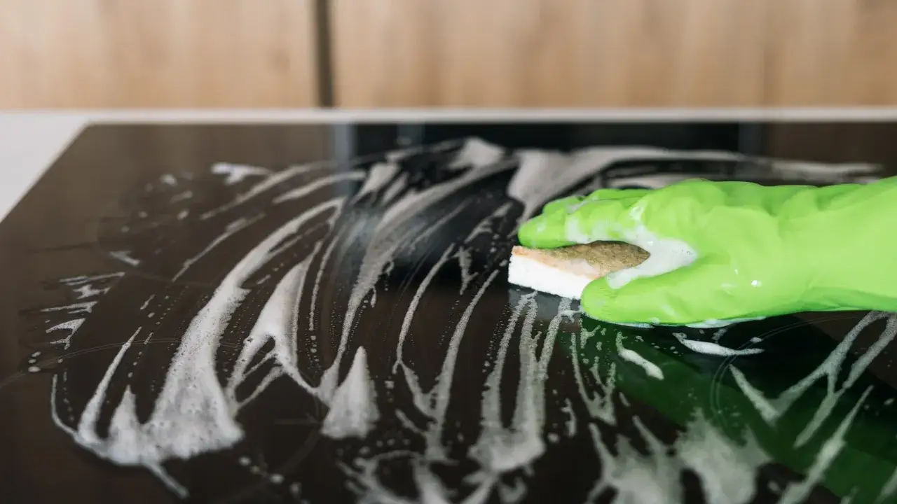 Gr&uuml;ne Handschuhe reinigen mit einem Schwamm und Schaum das Ceranfeld.