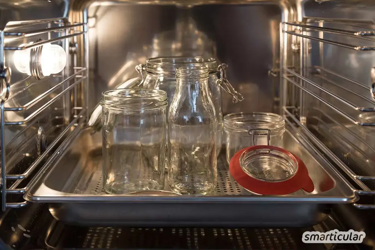 Mehrere leere Gl&auml;ser und Flaschen stehen auf einem Blech im Backofen, bereit zum Sterilisieren.