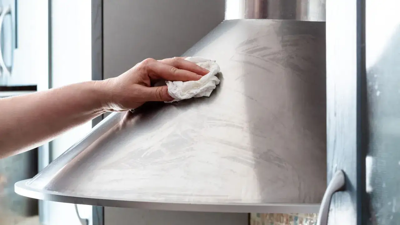 Hand reinigt klebrige Dunstabzugshaube mit einem Tuch.