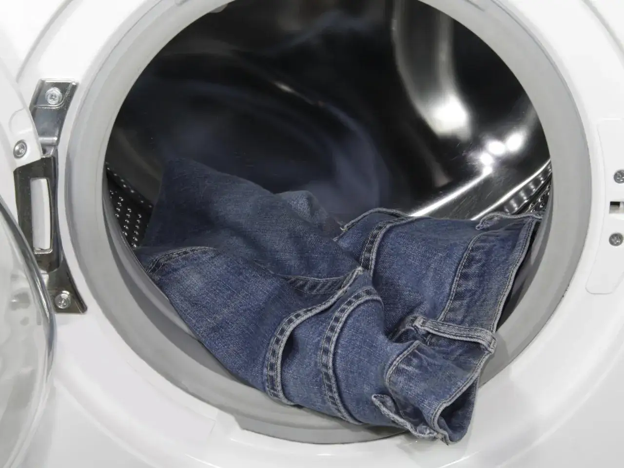 Blaue Jeans liegen in der Trommel einer Waschmaschine, bereit, um sie einlaufen zu lassen.